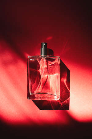 Transparent bottle of perfume on a red background. Fragrance presentation with daylight. Trending...
