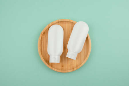 Two plastic white tubes for cream or lotion on the wooden podium. Top view on light mint green...