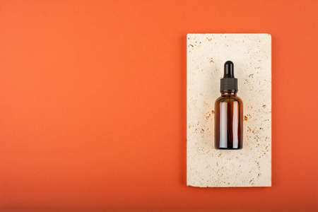 Amber glass dropper bottle with black lid on stone plate. Trending concept in natural materials on terracotta color background. Presentation backdrop for text or advertising.の写真素材