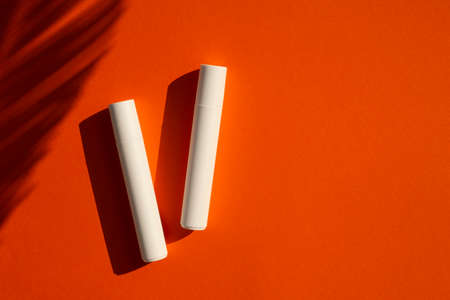 Two plastic white tubes for cream or lotion. Top view on orange background with palm leaves shadow.. Skincare cosmetic. Beauty concept for face body careの写真素材