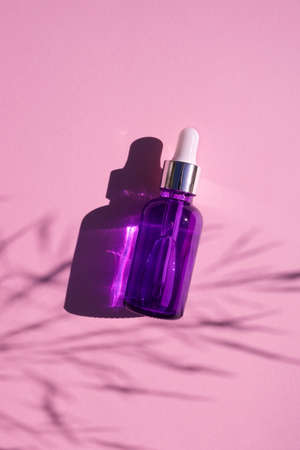 Purple glass dropper bottle with metallic lid. Top view on pink background with plant shadow. Skincare cosmetic. Beauty concept for face body careの写真素材