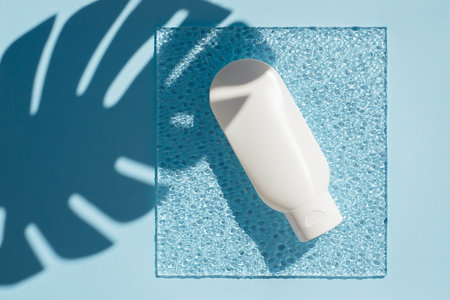 Plastic white tube for cream or lotion on an blue background and corrugated glass. Top view skincare...