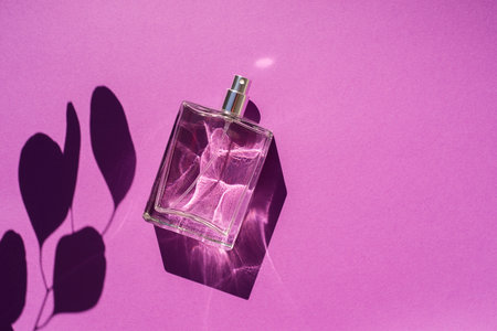 Transparent bottle of perfume on a purple background. Fragrance presentation with daylight. Trending...