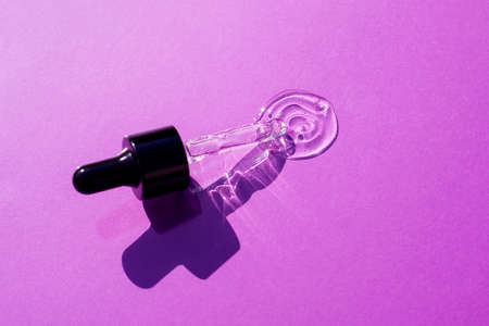 Open cap with dropper pipette with serum. Violet background with daylight and the appearance of the texture of the gel. Skincare products , natural cosmetic. Beauty concept for face and body careの写真素材