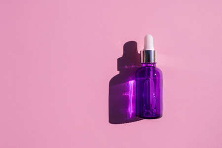 Purple glass dropper bottle with metallic lid. Top view on pink background. Skincare cosmetic. Beauty concept for face body careの写真素材