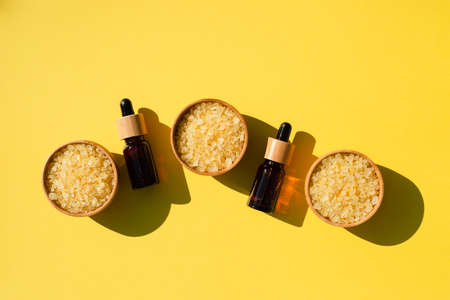 Wooden bowls filled with yellow bath sea salt and amber dropper bottles. Beauty treatment for spa and wellness. Skincare natural cosmetic concept for body care. Place for textの写真素材