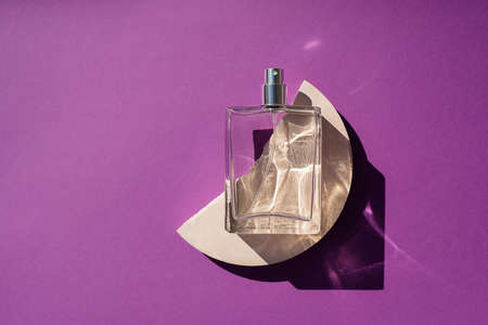 Transparent bottle of perfume on a podium on a purple background. Fragrance presentation with daylight. Trending concept in natural materials with plant shadow. Womens and mens essence.の写真素材