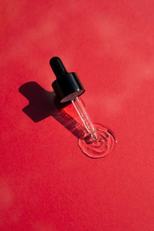 Open cap with dropper pipette with serum. Red background with daylight and the appearance of the texture of the gel. Skincare products , natural cosmetic. Beauty concept for face and body careの写真素材