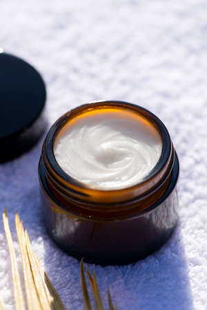 Open amber glass jar with dry palm and the appearance of the cream texture against the background of a white towel. Skincare products , natural cosmetic. Beauty concept for face body careの写真素材