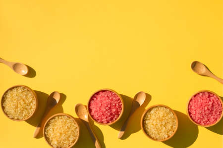 Wooden spoons and bowls filled with pink and yellow bath sea salt. Beauty treatment for spa and wellness. Skincare natural cosmetic concept for body care. Top view background. Place for textの写真素材