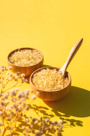 Wooden bowls with a spoon filled with yellow bath sea salt. Beauty treatment for spa and wellness with dry plants and shadows. Skincare natural cosmetic concept for body careの写真素材