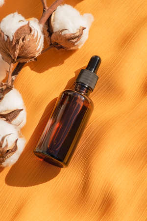 Amber glass dropper bottles with black lid with cotton flowers on yellow fabric background. Skincare cosmetic. Beauty concept for face body careの写真素材