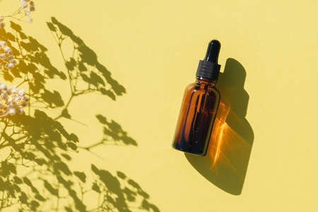 Amber glass dropper bottle with black lid. Top view on yellow background with plant shadow. Skincare cosmetic. Beauty concept for face body careの写真素材