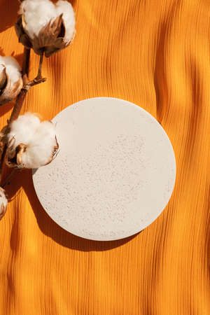 White podium for product presentation with cotton flowers on yellow fabric background. Empty cylindrical platform for cosmetic. Mockup with concrete circle and copy space.の写真素材