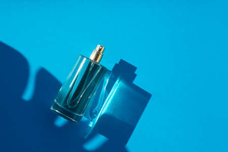 Transparent bottle of perfume on a blue background. Fragrance presentation with daylight. Trending concept in natural materials with palm leaves shadow. Womens and mens essence.の写真素材