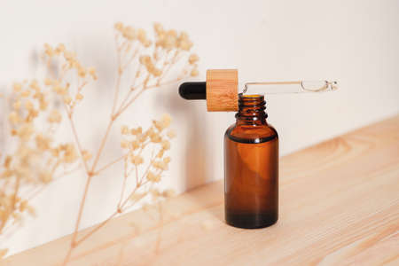 Open bottle with dropper pipette with serum or essential oil on natural wooden background with daylight. Skincare products , natural cosmetic with with dry plants. Beauty concept for face body careの写真素材