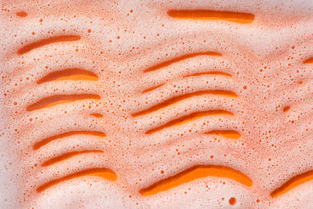 Foam on an orange background. Soapy liquid texture with bubbles. Natural sunshine and shadows....
