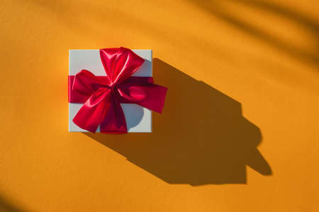 White gift box with red ribbon on a yellow background. Valentines day backdrop. Flat lay style with minimalistic design. Template for banner or party invitationの写真素材