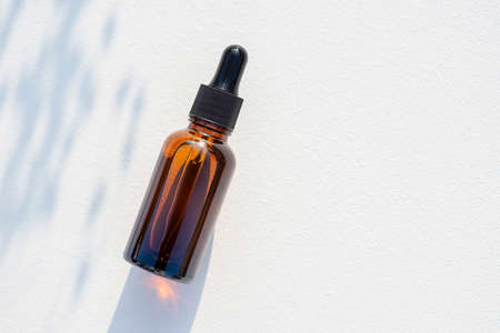 Amber glass dropper bottle with black lid. Top view on white background with plant shadow. Skincare cosmetic. Beauty concept for face body careの写真素材