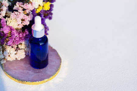 Blue glass dropper bottle on white background with dry flowers. Container mockup with cosmetic oil...