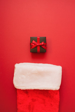 Black gift with a red bow in red Santas socks. Packaging and preparation of gifts for the celebration. Christmas New Year backdropの写真素材