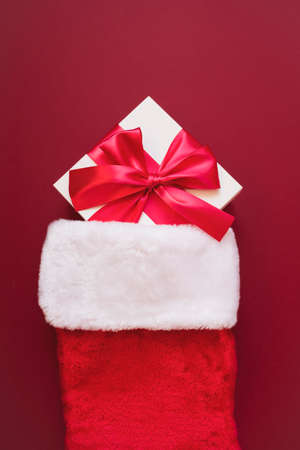 White gift with a red bow in red Santas socks. Packaging and preparation of gifts for the...