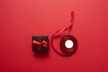 Black gift with a bow and ribbon on a red background. Packaging and preparation of gifts for the celebration. Christmas New Year backdropの写真素材