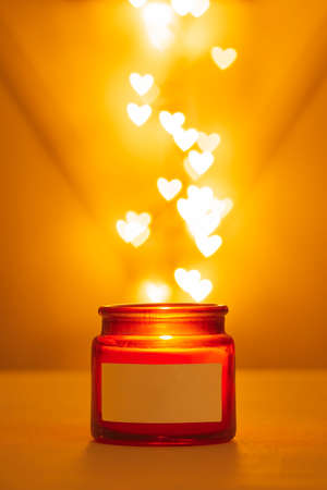 Glass red-brown jar a burning candle against the background of bokeh lights in the form of hearts....