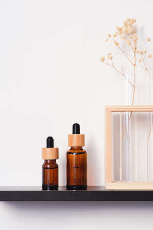 Amber glass dropper bottles with bamboo lid on the black shelf. Skincare concept on white wall background. Spa natural cosmetic concept for face body careの写真素材
