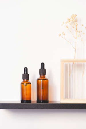 Amber glass dropper bottles with black lid on the shelf. Skincare concept on white wall background. Spa natural cosmetic concept for face body careの写真素材