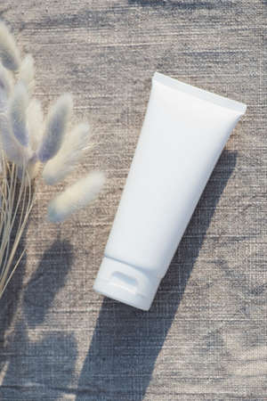 Plastic white tube for cream or lotion with dry plants on natural fabric background. Skincare products . Spa natural cosmetic concept for face body careの写真素材
