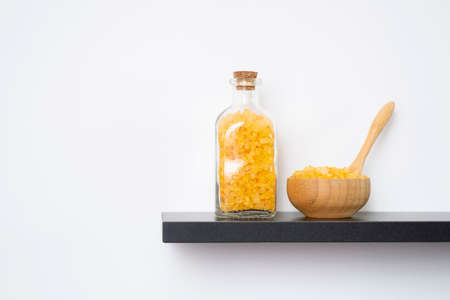 Wooden spoon, bowl and bottle filled with yellow bath sea salt on the black shelf. Beauty treatment for spa and wellness. Skincare natural cosmetic concept for body care.の写真素材