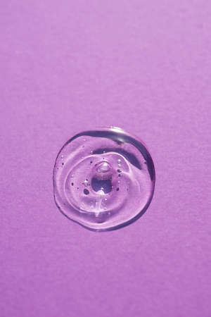 Transparent drop of cosmetic product serum gel. Liquid texture with bubbles on purple background in top view. Natural skincare products. Beauty concept for face and body careの写真素材