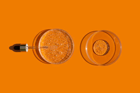 Open cap with dropper pipette with serum and petri dish on orange background. Transparent container...