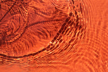Rippled water light orange backdrop. Background with sun reflection for cosmetic concept....