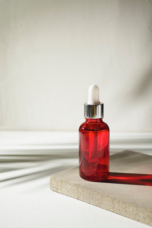 Red glass bottle with dropper pipette with serum or essential oil on concrete plate for product presentation with palm leaves shadow. Skin care cosmetic. Beauty concept for face body careの写真素材