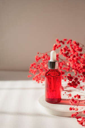 Red glass bottle with dropper pipette with serum or essential oil on concrete plate for product presentation with dry flowers. Skin care cosmetic. Beauty concept for face body careの写真素材