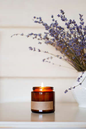 Glass red-brown jar a burning candle on the on a nightstand with lavender flowers. Home comfort...