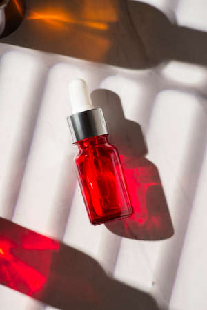 Red glass bottles with dropper pipette with serum or essential oil on a white background. Skincare cosmetic with beautiful shadows. Beauty concept for face body care.の写真素材