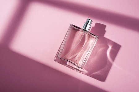 Transparent bottle of perfume on a pink background. Fragrance presentation with daylight. Trending concept in natural materials with window shadow. Womens essence.の写真素材