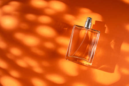 Transparent bottle of perfume on a orange background. Fragrance presentation with daylight. Trending concept in natural materials with window shadow. Womens essence.の写真素材