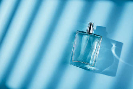 Transparent bottle of perfume on a blue background. Fragrance presentation with daylight. Trending concept with window shadow. Womens essence.の写真素材