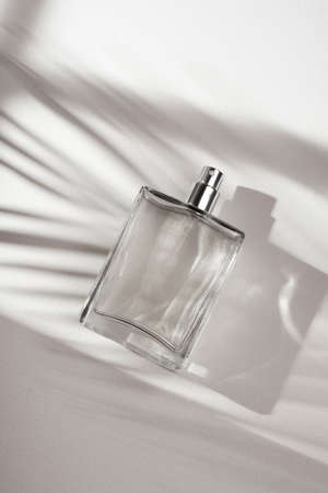 Transparent bottle of perfume on a white background. Fragrance presentation with daylight. Trending concept in natural materials with palm leaves shadow. Womens and mens essence.の写真素材