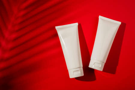 Plastic white bottles for cream or lotion on a red background. Skincare cosmetic with beautiful flowers shadows. Beauty concept for face body care.の写真素材