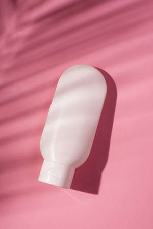 Plastic white tube for cream or lotion. Skin care or sunscreen cosmetic in top view on pink background with palm leaves shadow. Beauty concept for face careの写真素材