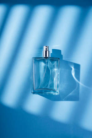 Transparent bottle of perfume on a blue background. Fragrance presentation with daylight. Trending...