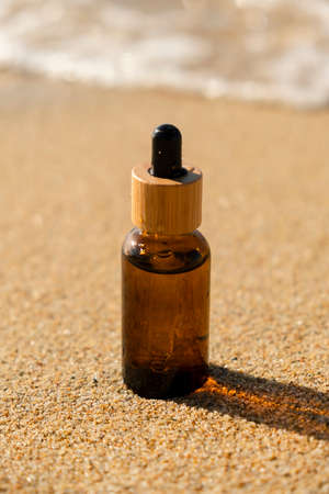 Amber glass bottle with dropper pipette with serum or essential oil on the sea sand. Skin care cosmetic with beautiful shadows. Beauty concept for face body careの写真素材