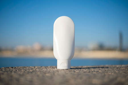 Plastic white tube for cream or lotion on a blurred background of the sea and the beach. Skin care cosmetic with beautiful shadows. Beauty concept for face body care.の写真素材