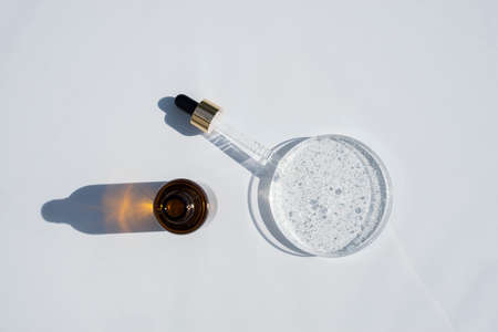 Open dropper bottle and cap with dropper pipette with serum and petri dish on light background....