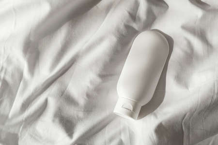 Plastic white tube for cream or lotion on light fabric background. Skin care cosmetic presentation with daylight and beautiful shadow. Beauty concept for face body care.の写真素材